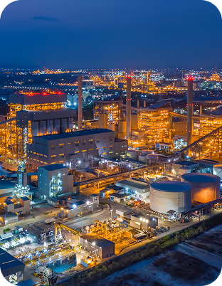 Industrial plant with multiple lit buildings and storage tanks at night under a dark blue sky.